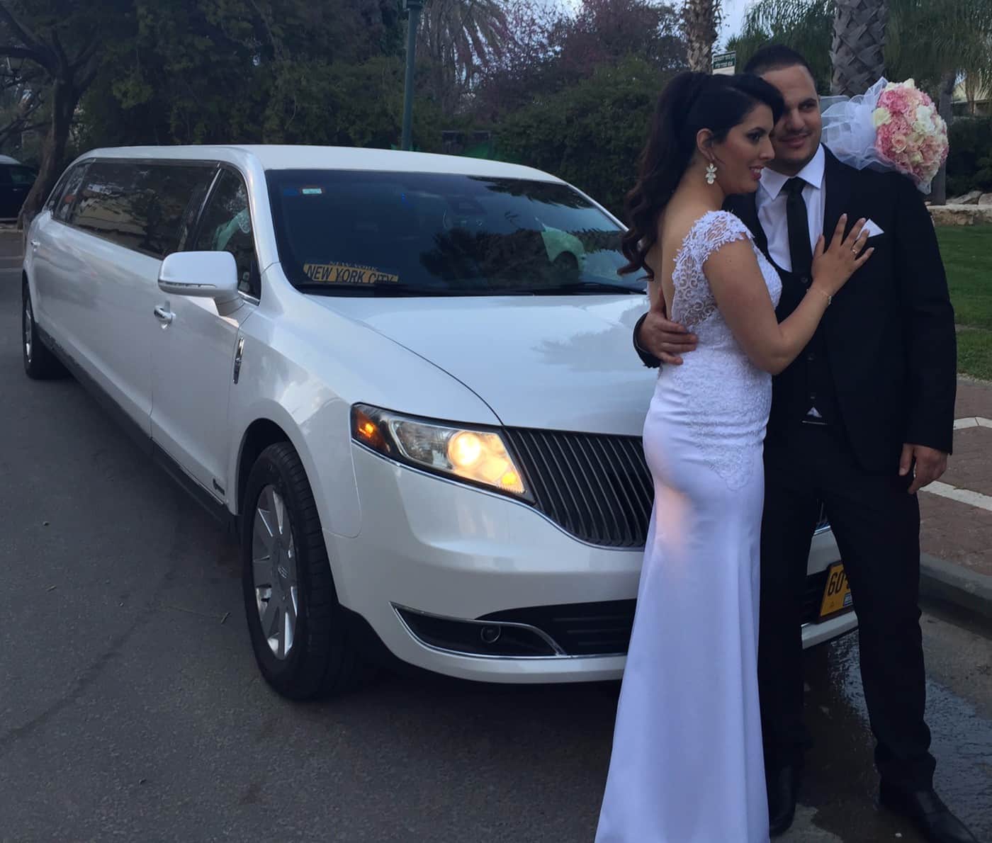 חתן וכלה מצטלמים ליד לימוזינה לבנה יוקרתית ביום החתונה חתן וכלה מצטלמים ליד לימוזינה לבנה יוקרתית ביום החתונה